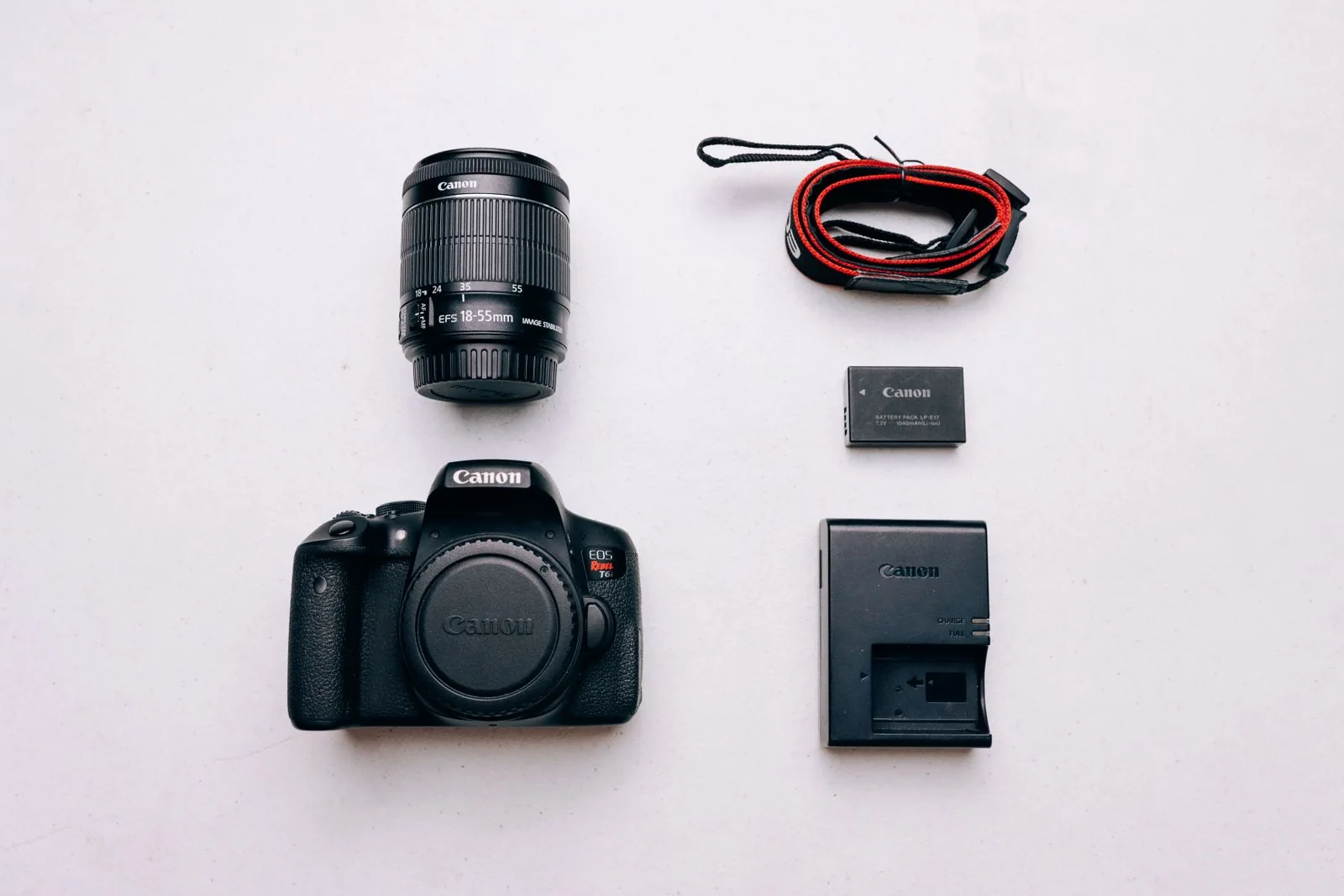 A camera body, zoom lens, strap, battery and charger arranged on a light tabletop.
